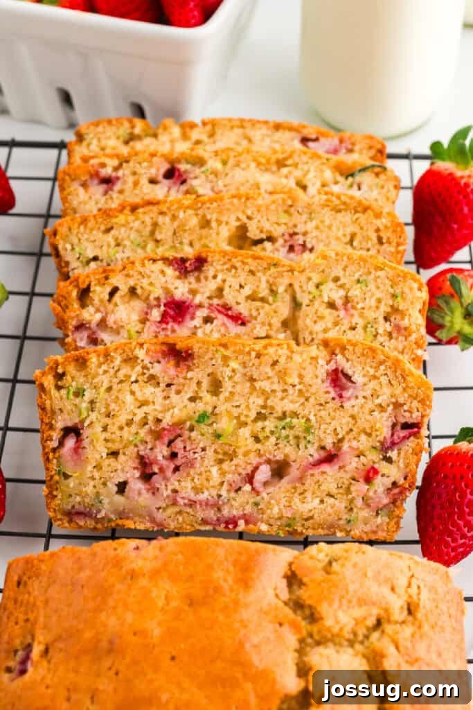 A freshly baked loaf of Strawberry Zucchini Bread cooling on a wire rack, surrounded by glistening fresh strawberries and a bottle of milk, ready to be enjoyed.