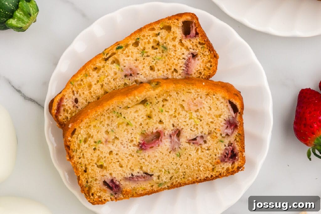 An overhead shot featuring two perfectly sliced pieces of Strawberry Zucchini Bread on a white plate, showcasing the delicious bits of fruit and zucchini throughout the moist crumb.