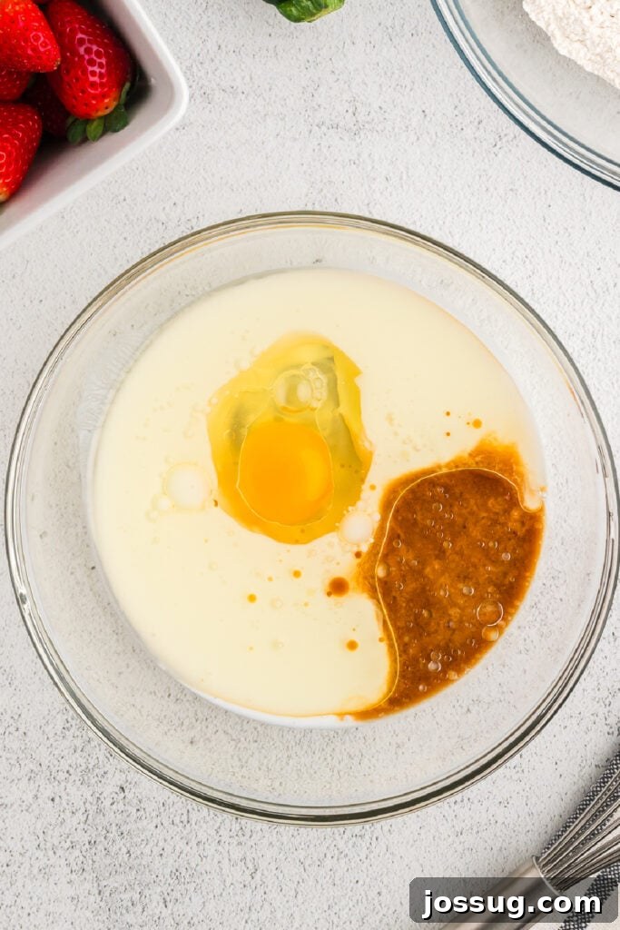 A glass mixing bowl holds a clear liquid mixture of buttermilk, egg, vegetable oil, and vanilla extract, ready for whisking.