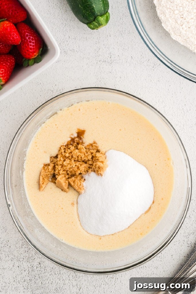 Granulated sugar and light brown sugar are sprinkled into the bowl of whisked wet ingredients, ready to be fully incorporated.