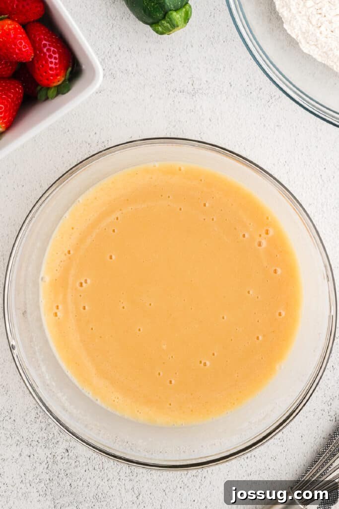 The wet mixture and sugars are fully combined into a smooth, light brown batter, glistening in the glass bowl.