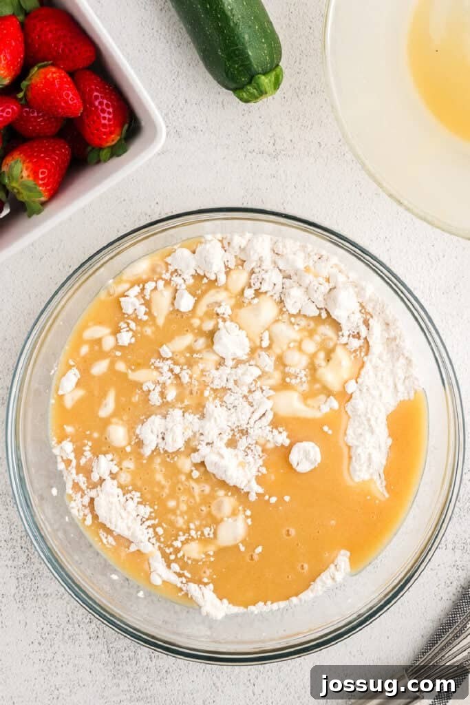 The wet and dry ingredients have just been combined in a large glass bowl, with a few flour clumps still visible, indicating the perfect stage before overmixing.