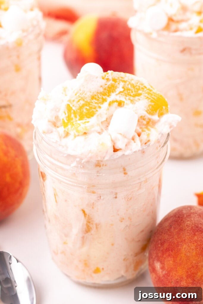 Mason jar filled with peach fluff salad next to fresh peaches, highlighting its refreshing appeal.