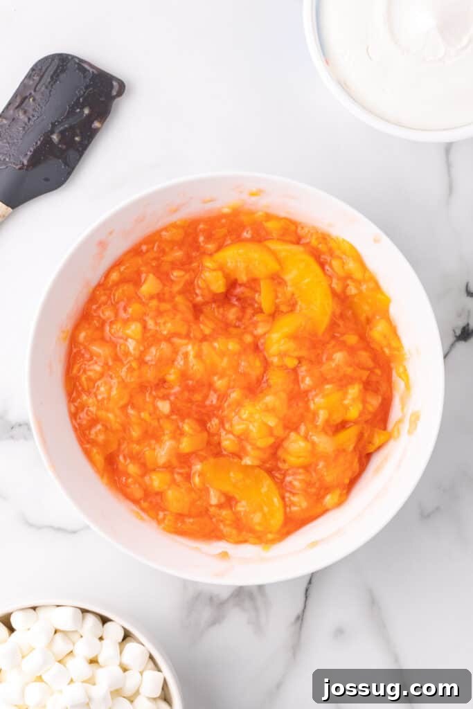 Peach fluff mixture of gelatin, pie filling, and pineapple partially stirred, showing the vibrant colors.