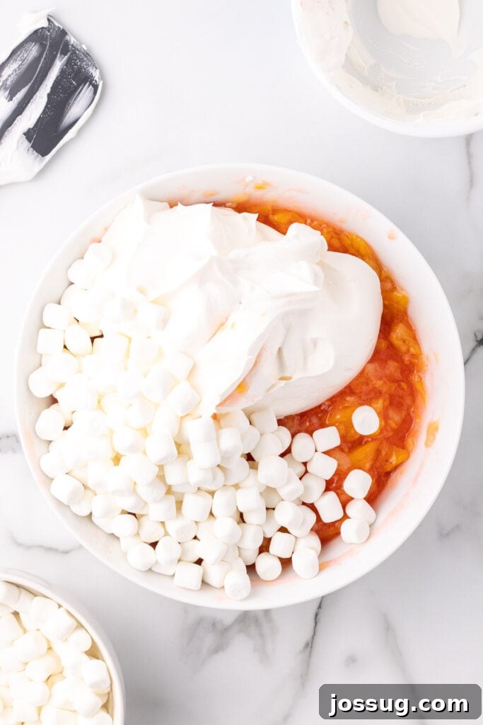 Whipped topping and mini marshmallows added to the peach fluff mixture, ready to be folded.