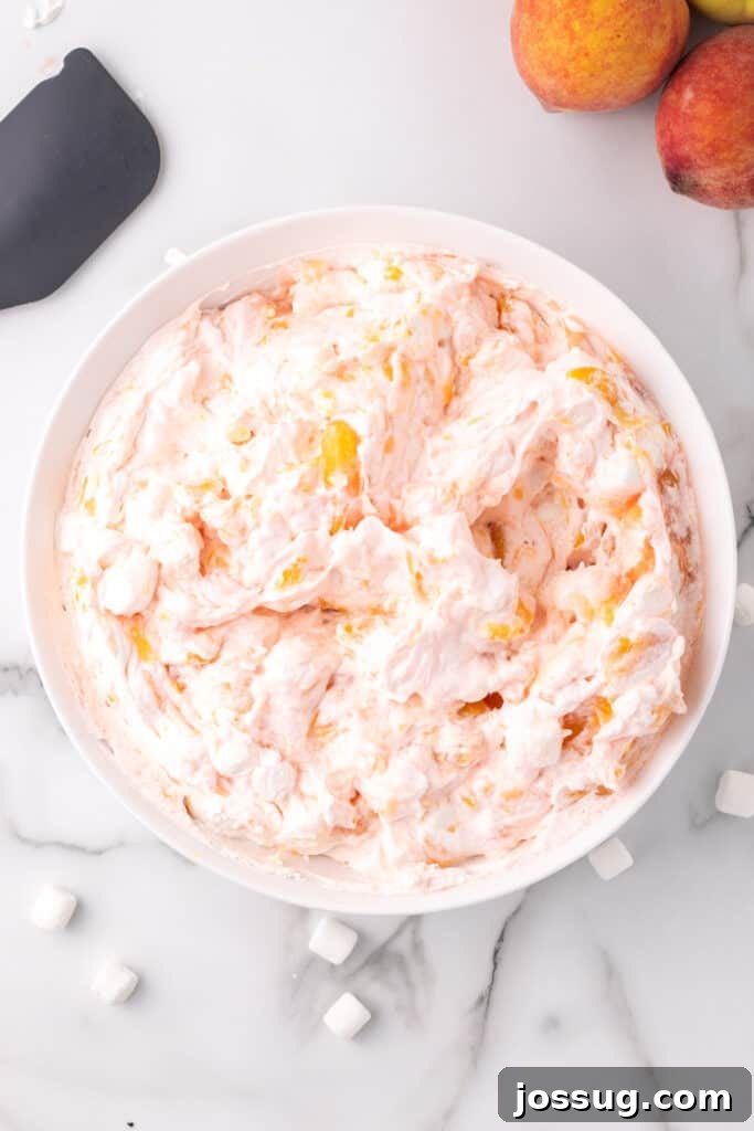Fully combined peach fluff salad in a white mixing bowl, showcasing its creamy, fluffy texture.