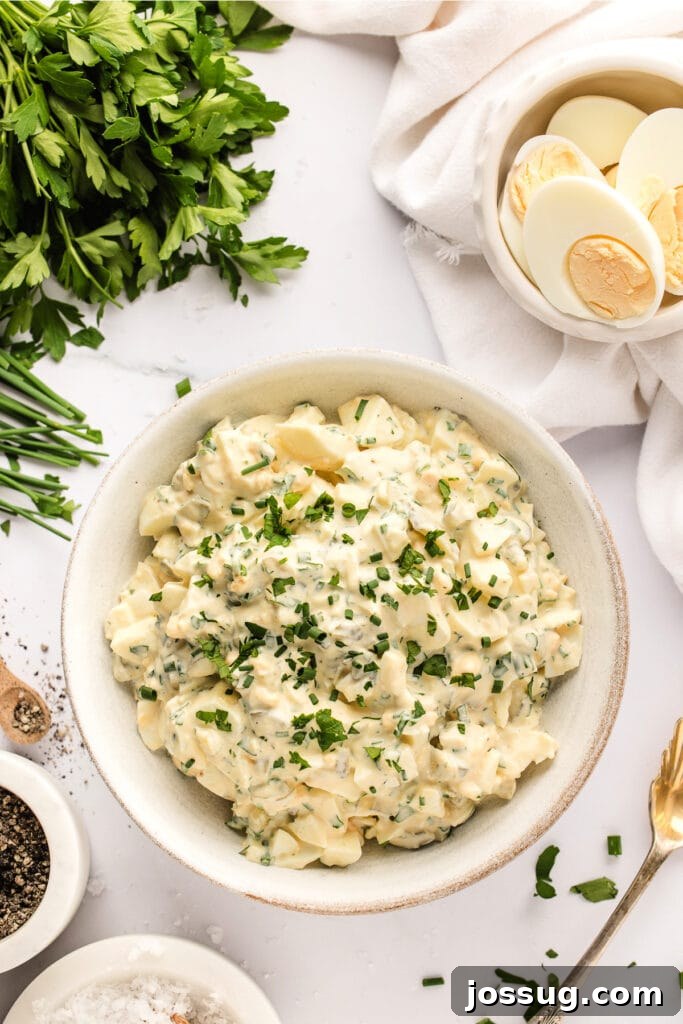 Looking down onto a bowl of freshly made herbed egg salad, garnished with fresh herbs and a slice of dill pickle