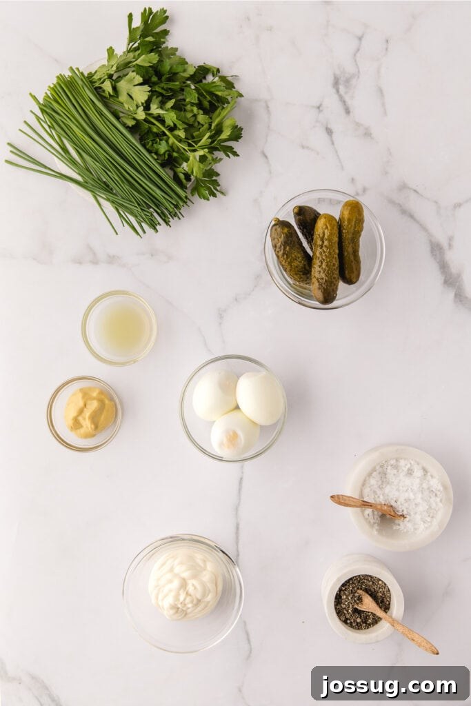 A collection of fresh ingredients laid out on a wooden board, including hard-boiled eggs, fresh parsley, chives, dill pickles, mayonnaise, and Dijon mustard