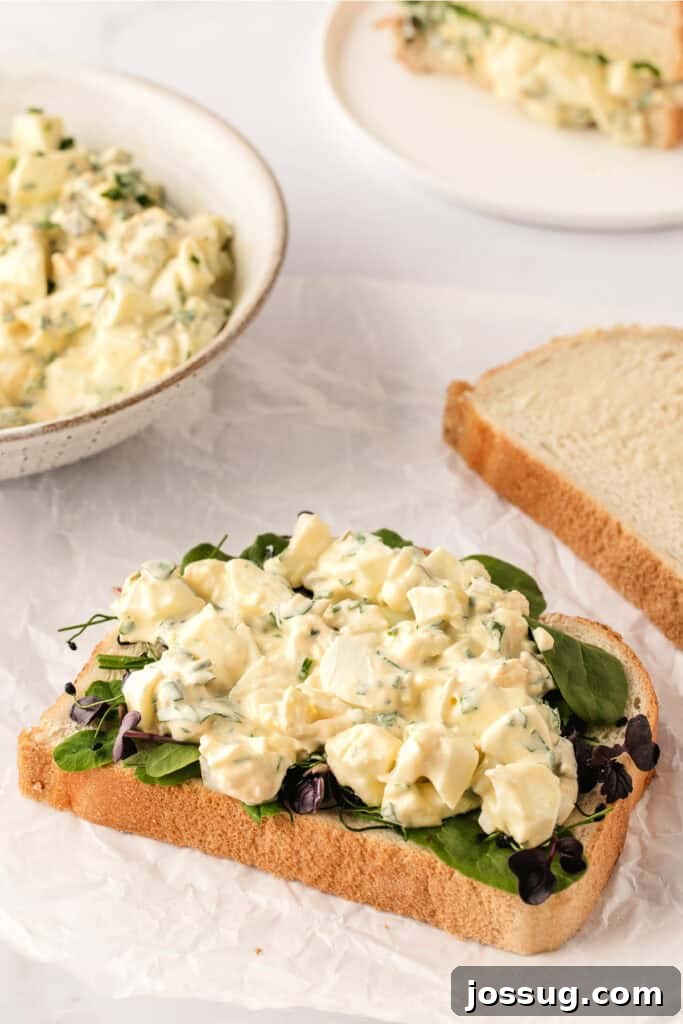 Herbed egg salad generously spread on a slice of bread with fresh lettuce, ready to be made into a sandwich.