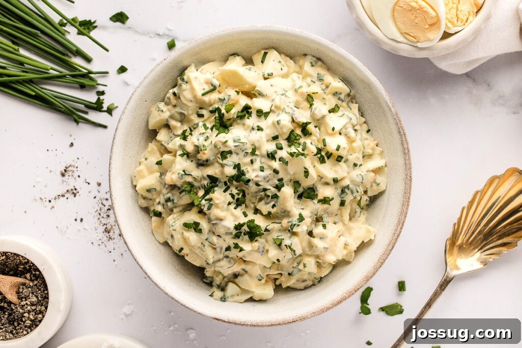 A large bowl of herbed egg salad, garnished beautifully with fresh herbs and a sprinkle of black pepper, ready to be served at a gathering or picnic.