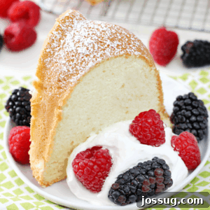 A slice of Old-Fashioned Cream Cheese Pound Cake, garnished with powdered sugar, fresh berries, and whipped cream, presented on a white plate with a fork.