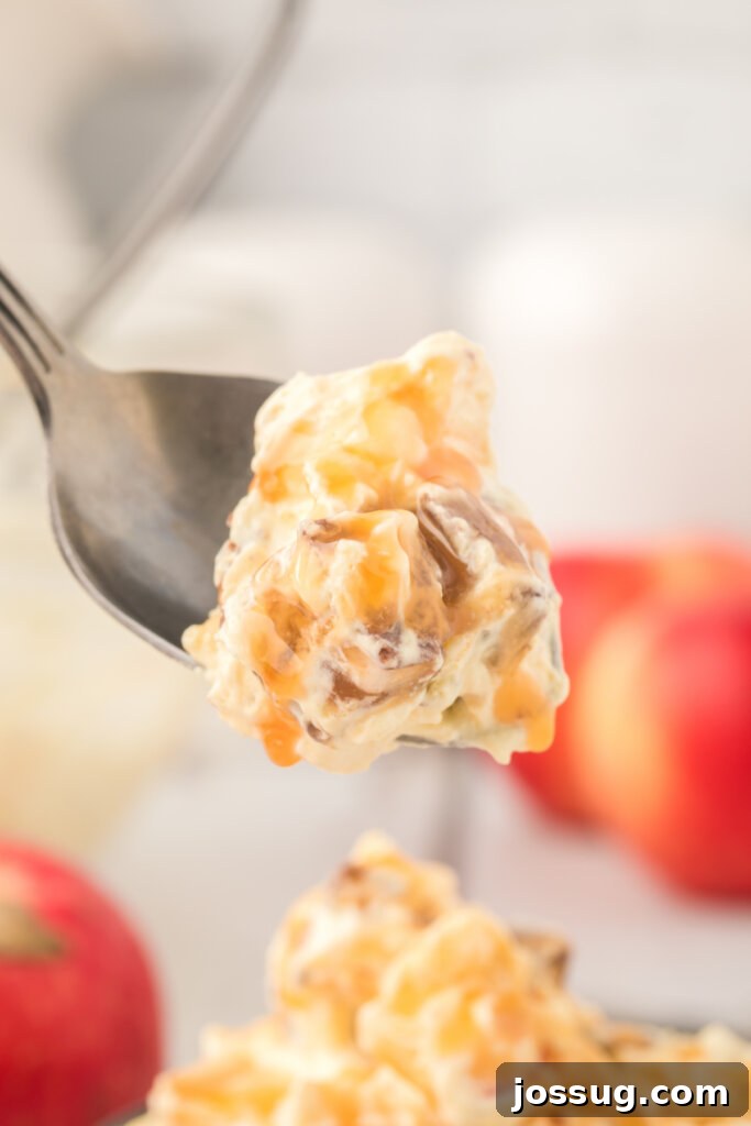 A fork lifting a bite of Caramel Apple Snickers Salad, highlighting the texture and gooey caramel.