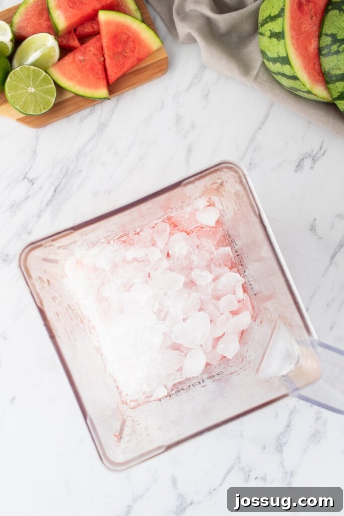 Crimson Wave Margarita 8 Ice cubes being added to a blender already containing blended watermelon and lime, on a white surface