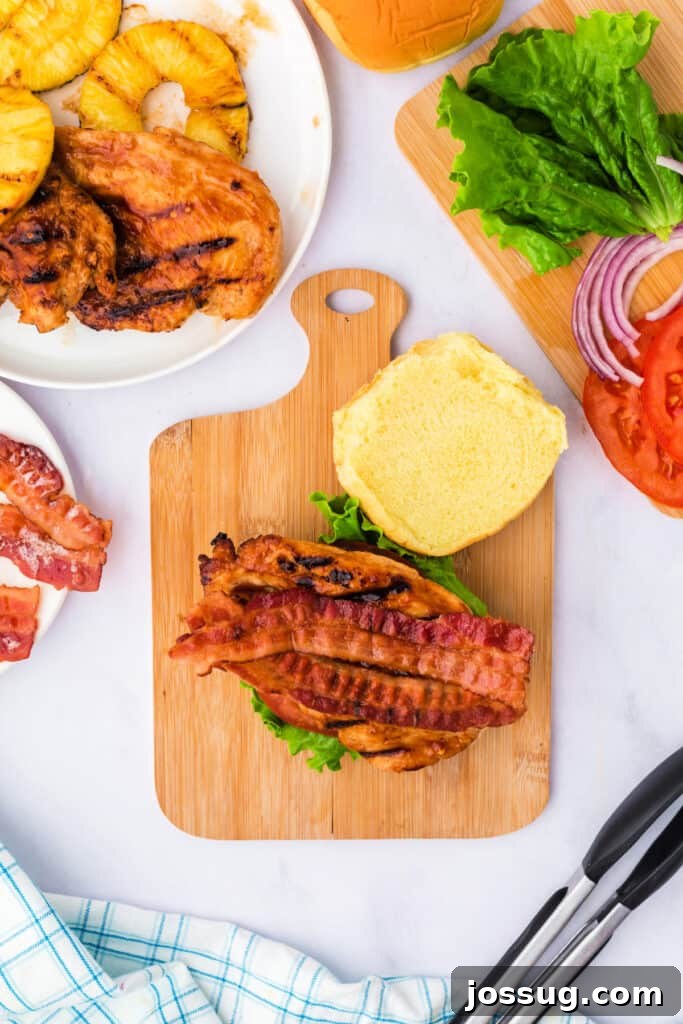 Placing crispy bacon strips over the grilled chicken, adding a smoky, savory crunch to the sandwich.