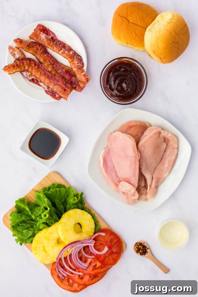 Ingredients for grilled Hawaiian chicken sandwich including bacon, buns, BBQ sauce, chicken breasts, soy sauce, lettuce, pineapple, tomato, and red onion, all laid out on a wooden surface.