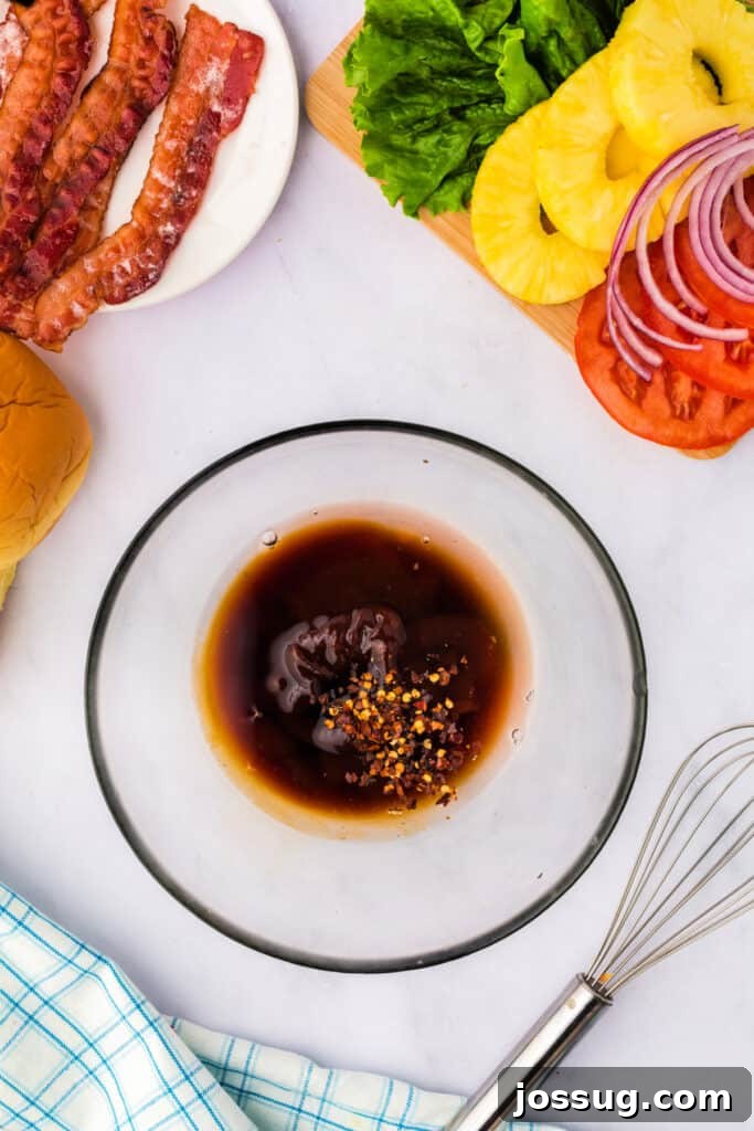 Overhead view of marinade ingredients in a bowl surrounded by bacon, lettuce, pineapple, tomato, and sandwich buns, ready for mixing.