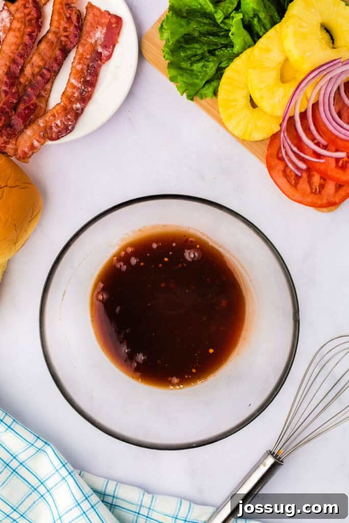 Marinade mixed together in a glass bowl, showcasing a smooth, rich sauce, with bacon, lettuce, pineapple, tomato, and buns nearby.