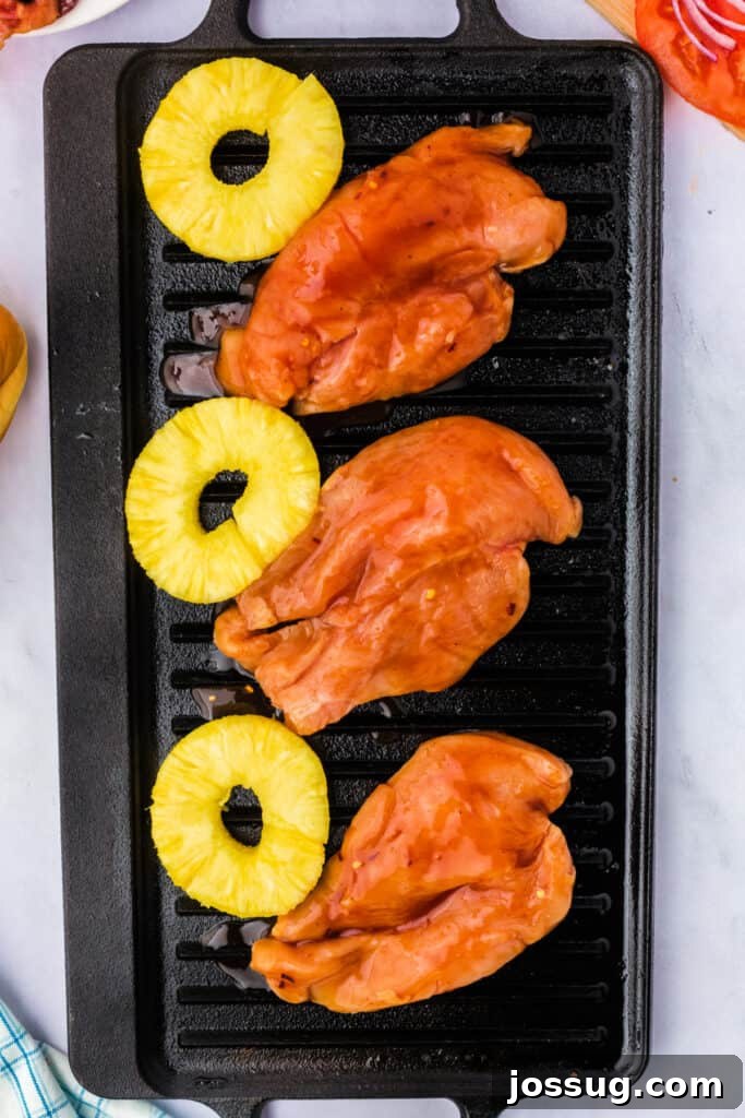 Marinated chicken breasts and pineapple slices grilling on a stovetop grill pan, showing early charring.