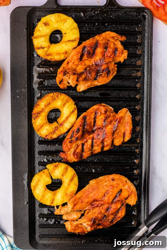 Perfectly grilled chicken breasts and pineapple slices with visible char marks, cooked to perfection on a grill pan.