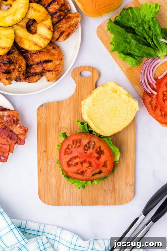 Assembling the sandwich, starting with crisp lettuce and juicy tomato slices layered on the bottom bun.