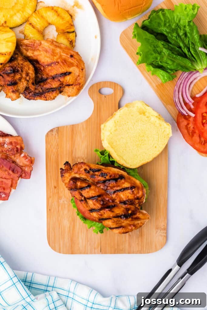 Adding a perfectly grilled chicken breast on top of the fresh lettuce and tomato on the sandwich.