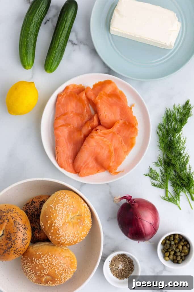 Ingredients laid out for smoked salmon bagels including bagels, cream cheese, smoked salmon, fresh dill, English cucumber, red onion, lemon wedges, capers, and seasonings, on a rustic wooden board.