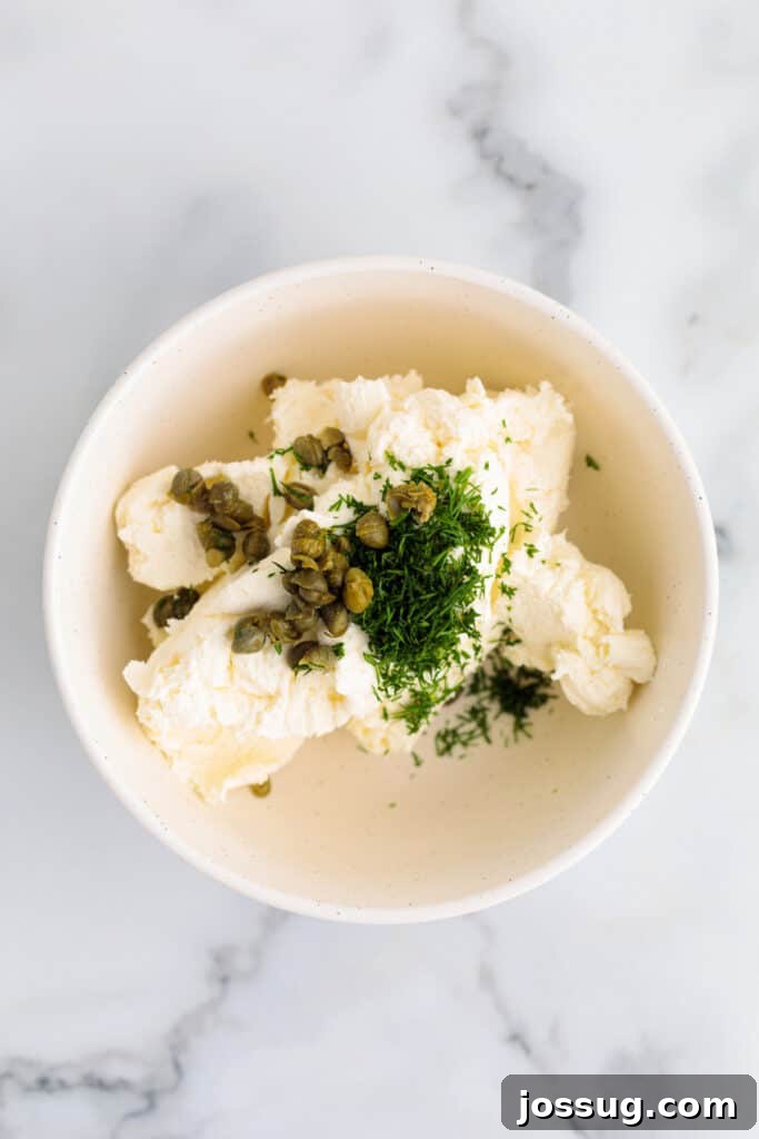 Cream cheese in a bowl with capers and chopped dill before mixing.