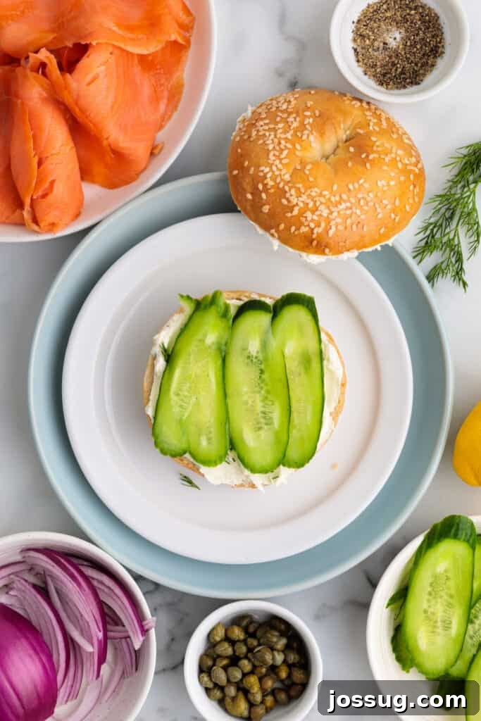 Bagel half with cream cheese topped with fresh cucumber slices, ready for the next layer.
