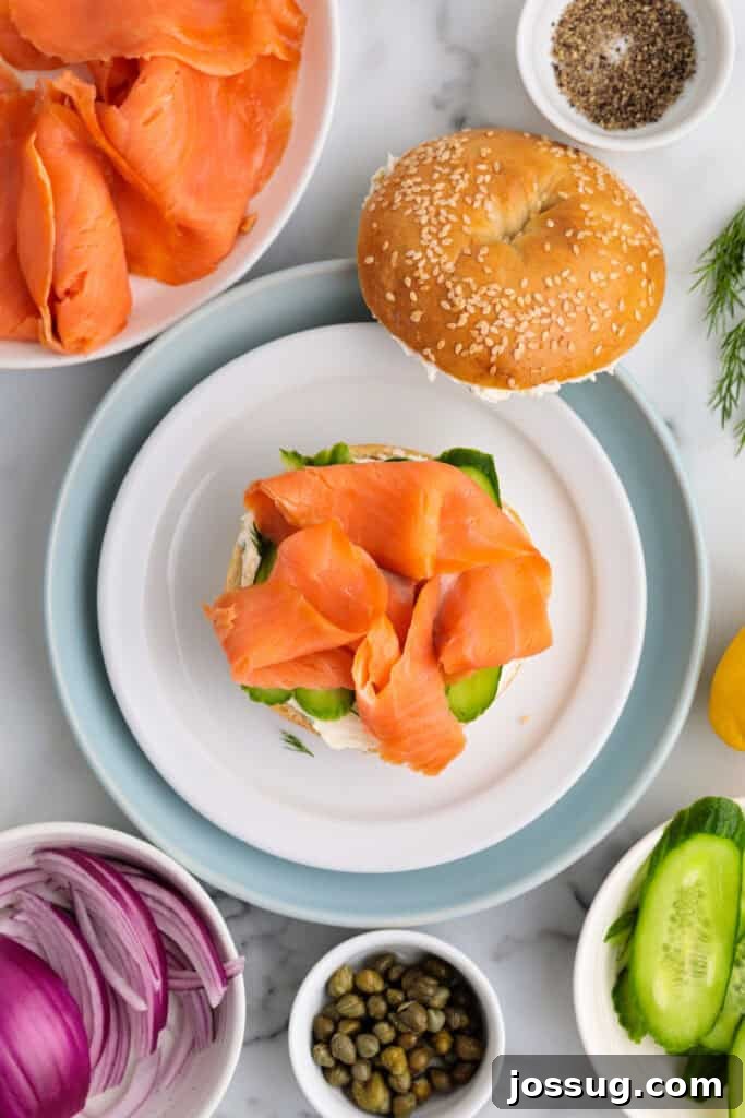Cucumber-topped bagel with a generous portion of smoked salmon being layered on.