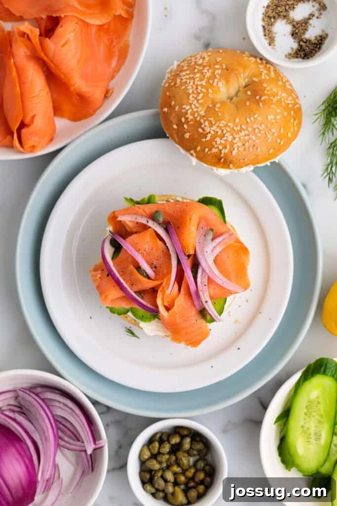 Smoked salmon bagel with red onion slices and capers added, showing a near-finished build.