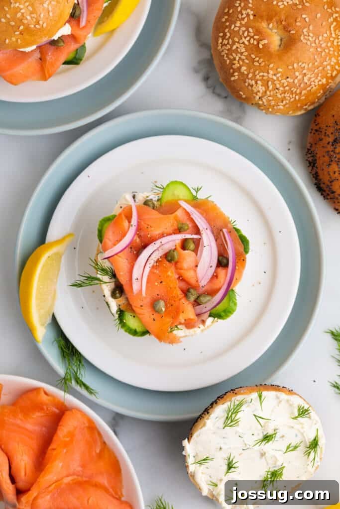 Open-faced smoked salmon bagel fully topped with cucumber, onion, capers, dill, and lemon wedge garnish.