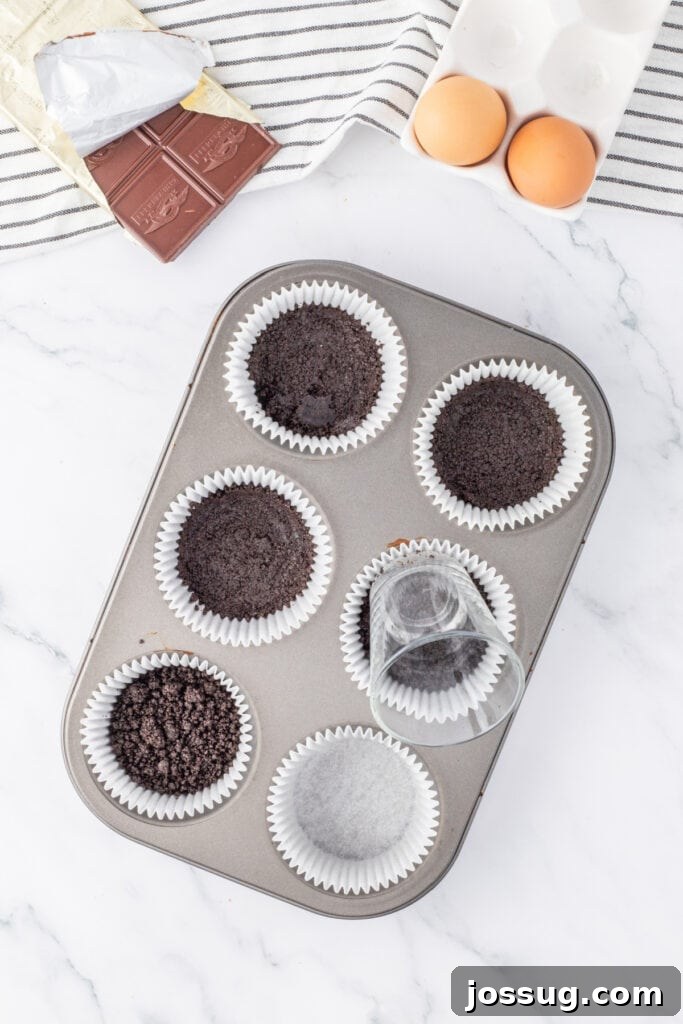 Pressing Oreo crust into liners using the bottom of a small glass in a muffin tin