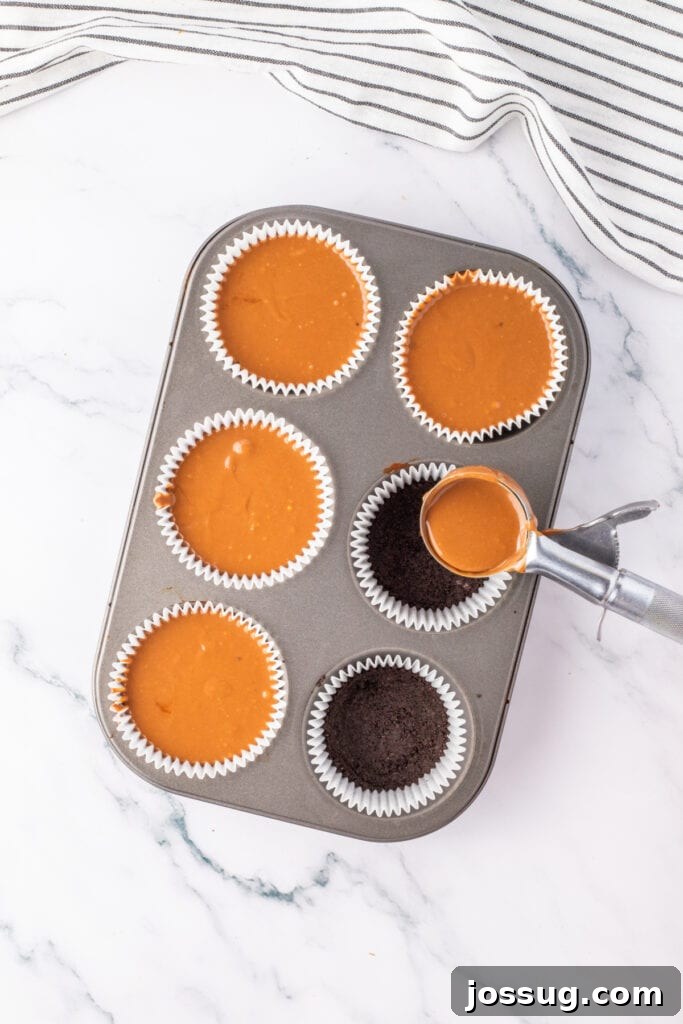 Filling liners with cheesecake batter and Oreo crust in a muffin tin using an ice cream scoop