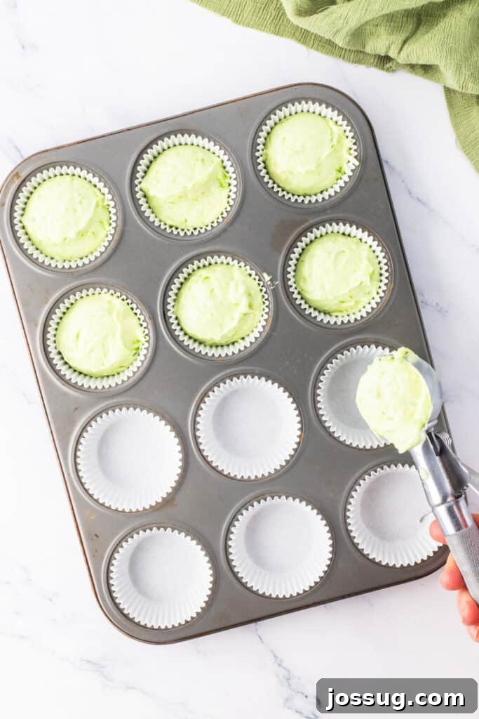 Cupcake batter with green tint being scooped into a lined muffin pan