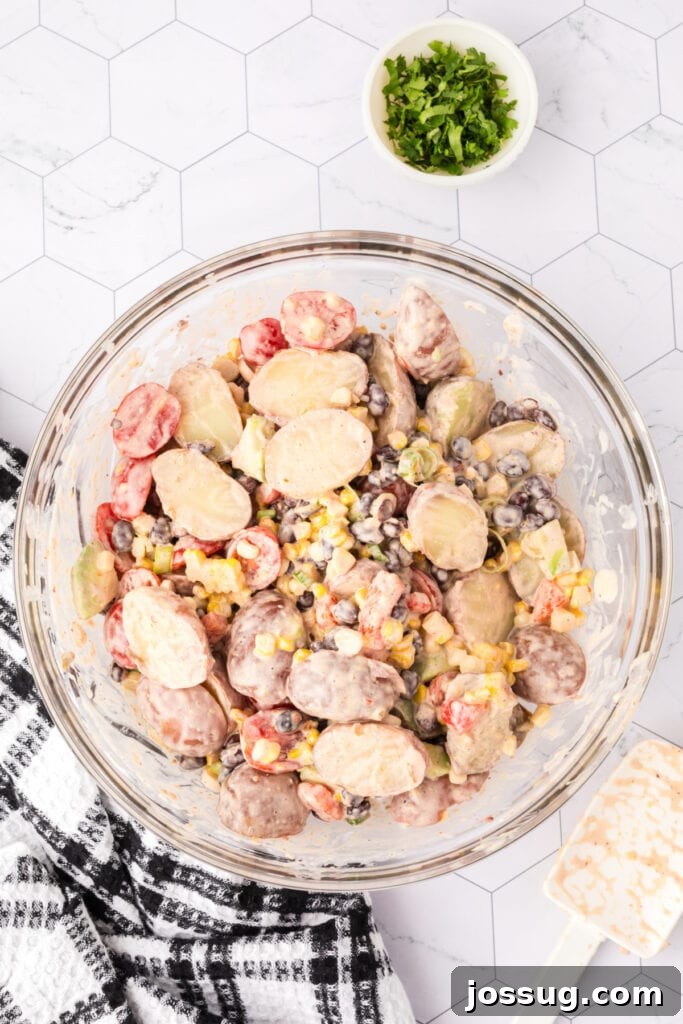 Mixed Southwest Potato Salad in a large glass bowl, coated in creamy dressing.