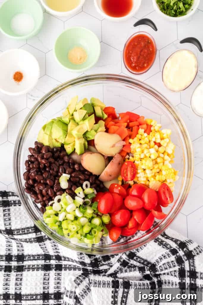 Large mixing bowl filled with potatoes, avocado, black beans, tomatoes, corn, and green onions.