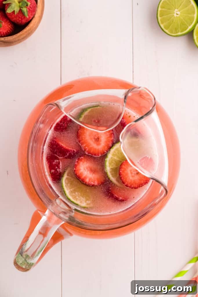 Blush Burst Cooler 11 Strawberry limeade garnished with fresh lime and strawberry slices in a clear glass pitcher, ready to be served.