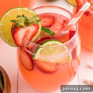 Close-up square image of a strawberry limeade glass with lime and strawberry slices and a pink striped straw, perfect for social sharing.
