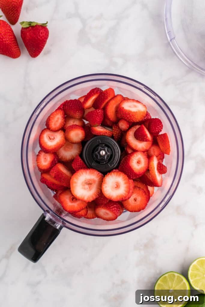 Blush Burst Cooler 4 Fresh sliced strawberries placed inside a food processor, ready for blending.