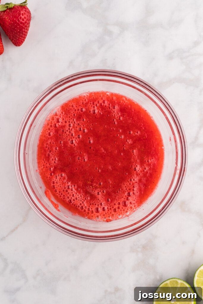 Blush Burst Cooler 7 Smooth, strained strawberry purée collected in a clear glass bowl, showcasing its vibrant color and silky texture.