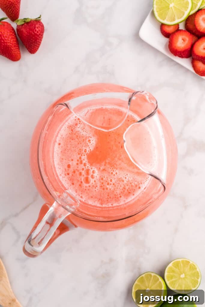 Blush Burst Cooler 10 Finished strawberry limeade mixture in a pitcher, appearing light pink and slightly frothy, indicating it's well-combined.