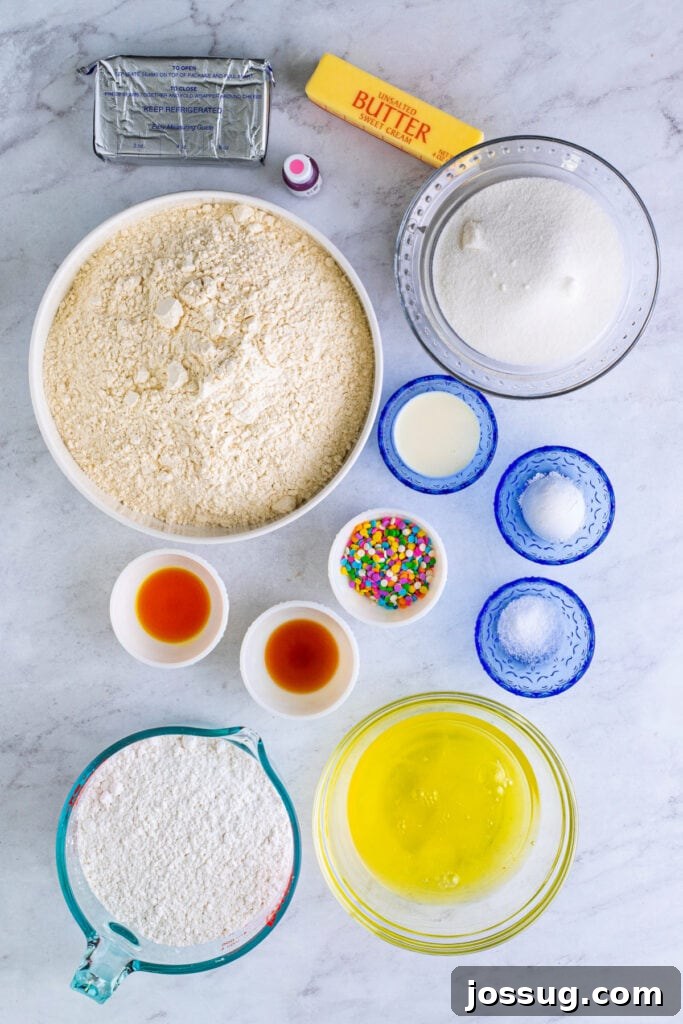 Gourmet Funfetti Sugar Cookies 3 Overhead view of cookie dough ingredients, including butter, sugar, flour, egg whites, sprinkles, and extracts on a marble background.