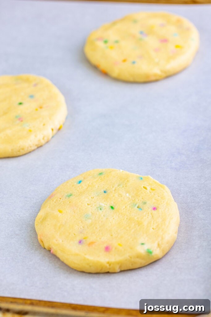 Gourmet Funfetti Sugar Cookies 5 Flattened cookie dough circles with visible sprinkles ready to bake on a parchment-lined baking sheet.