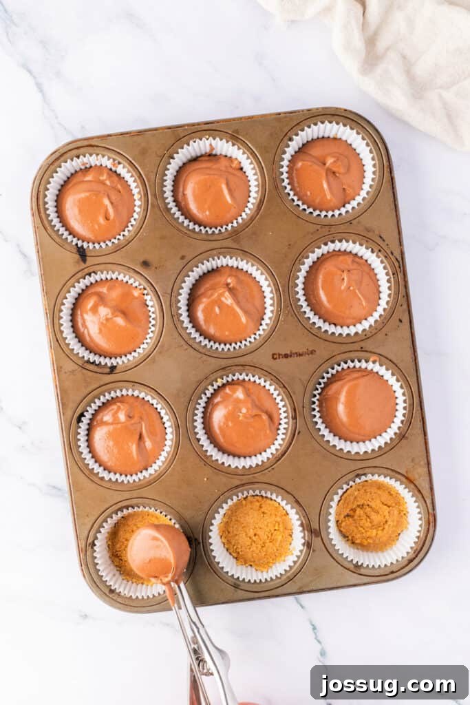 Effortless Chocolate Peanut Butter Cheesecake Bites 4 Chocolate cheesecake filling being spooned over graham cracker crust in a lined muffin pan. Some cups are already filled.