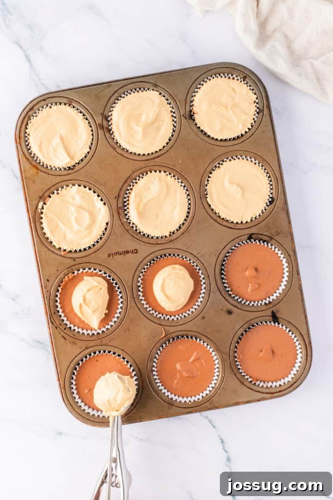 Effortless Chocolate Peanut Butter Cheesecake Bites 5 Peanut butter cheesecake layer being added over the chocolate layer in a lined muffin pan using a cookie scoop.