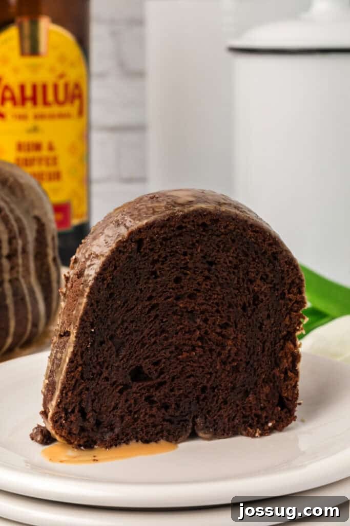 Decadent Kahlua Chocolate Bundt 2 A delectable slice of Chocolate KahlĂșa Bundt Cake resting on a pristine white plate, with a bottle of KahlĂșa softly blurred in the background, hinting at the cake's exquisite flavor.