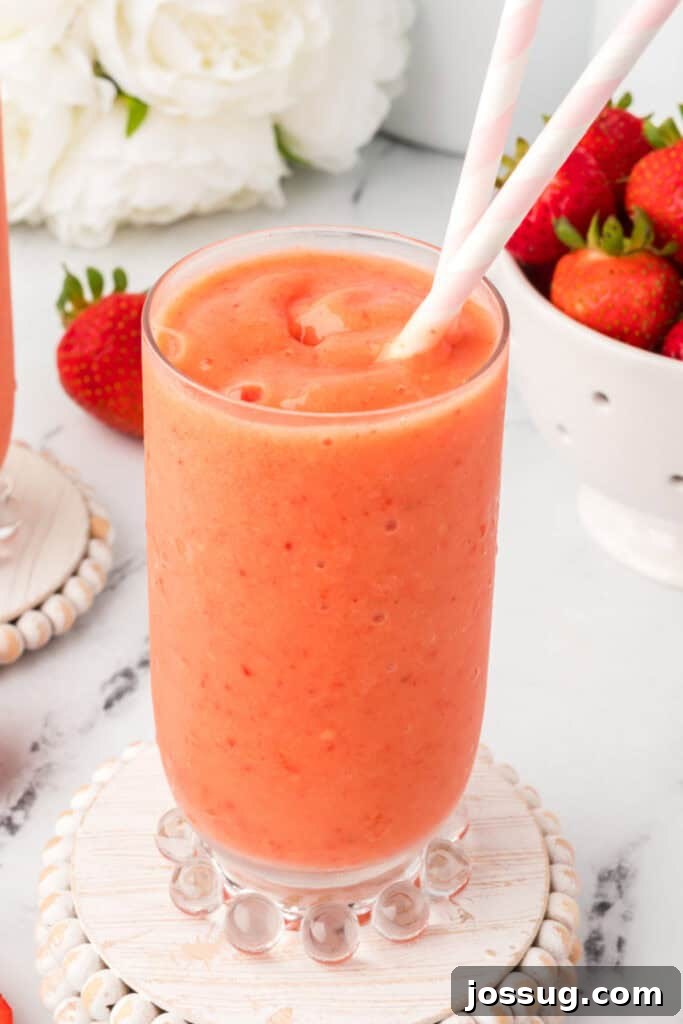 Tropical Ombre Smoothie 2 Single glass of vibrant sunrise sunset smoothie served on a decorative coaster, showcasing layers of strawberry and mango-pineapple.