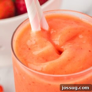 Close-up square image of sunrise sunset smoothie with pink and white striped straw.