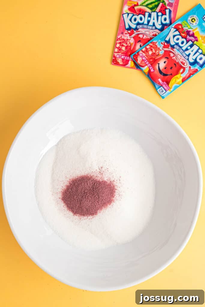 Sweet & Sour Zingers 5 A bowl of granulated sugar with a mound of vibrant Kool-Aid powder on top, with more Kool-Aid packets in the background.