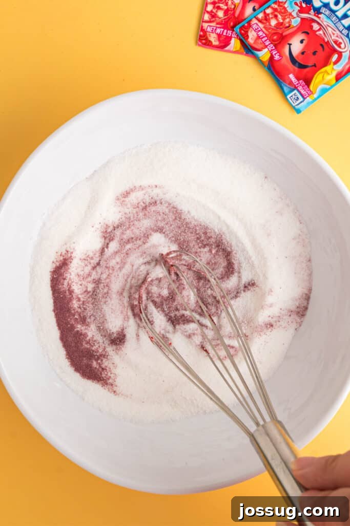 Sweet & Sour Zingers 6 A whisk vigorously mixing sugar and Kool-Aid powder in a white bowl, showing the dry ingredients combining.